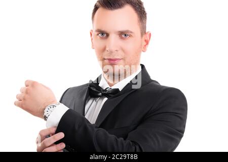 Portrait d'un jeune homme sûr et attrayant en costume noir avec noeud papillon, réglage des boutons de manchette sur sa chemise blanche, regardant l'appareil photo, isolé. Banque D'Images
