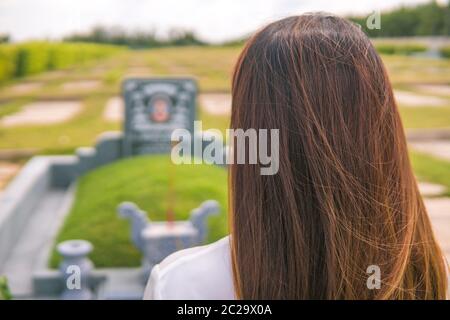 Une femme non identifiée éclaire l'encens, prosterant devant une tombe non identifiée dans le cimetière, jardin du sala, long Thanh, Vietnam. Concept de Banque D'Images