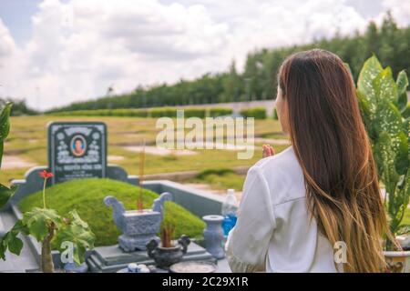 Une femme non identifiée éclaire l'encens, prosterant devant une tombe non identifiée dans le cimetière, jardin du sala, long Thanh, Vietnam. Concept de Banque D'Images