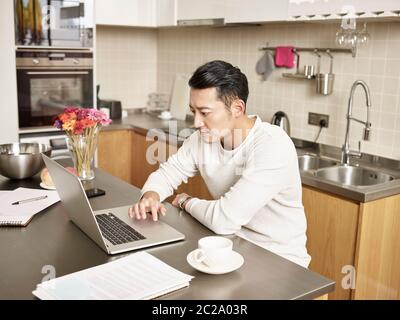 jeune homme d'affaires asiatique assis cuisine comptoir travaillant à la maison à l'aide d'un ordinateur portable Banque D'Images