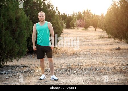 Portrait of Caucasian guy dans un azure t-shirt et short noir,qui se dresse sur un terrain difficile avant la course Banque D'Images