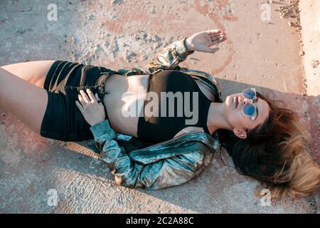 portrait d'une jeune fille brunette avec un beau corps en vêtements noirs et une veste argentée couché sur le toit et appréciant le Banque D'Images