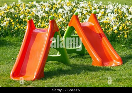 Magnifique terrain de jeux orange pour les petits enfants dans le jardin de printemps frais avec herbe verte et fleurs de jonquilles Banque D'Images