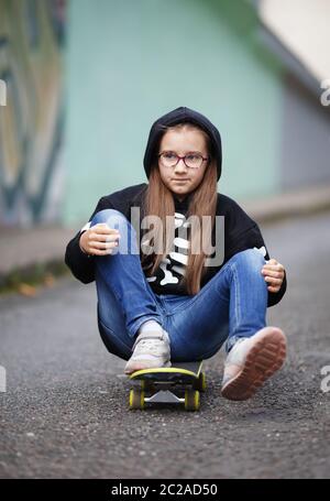 Girl se déplace sur roulettes. Enfant dans un sweat-shirt noir assis sur sa planche à roulettes. Tir vertical. Focus sélectif. Banque D'Images