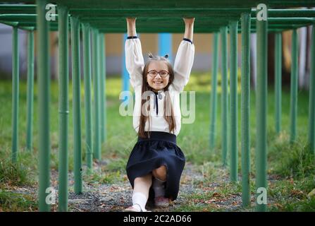 Cheerful girl enfant accroché sur la barre horizontale. Écolière est de s'amuser sur l'aire de jeux. Focus sélectif. Banque D'Images