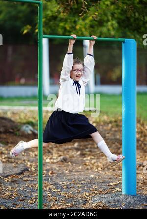 Heureux lycéenne est suspendu à la barre horizontale. Fille enfant s'amuser sur l'aire de jeux. Tir vertical. Focus sélectif. Banque D'Images