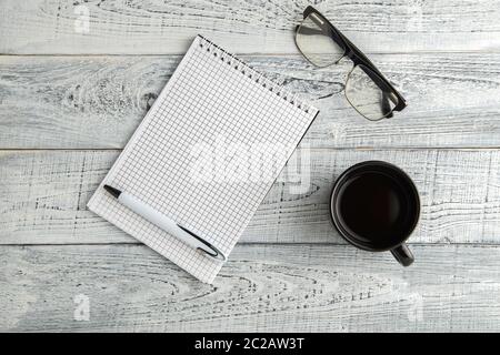 Carnet en papier, stylo et tasse de thé ou café et verres optiques sur fond de bois blanc vintage. Vue du dessus Banque D'Images