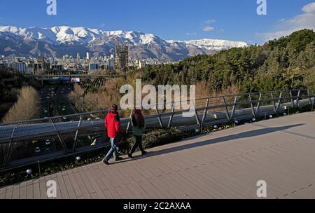 Le peuple iranien traverse le pont piétonnier moderne de Tabiat, jusqu'au parc Taleghani, avec les montagnes enneigées d'Alborz en arrière-plan, à Téhéran. Banque D'Images