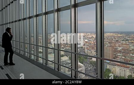 Homme d'affaires faisant face à une fenêtre supérieure avec vue sur la ville, depuis le gratte-ciel historique de Pirelli, à Milan. Banque D'Images