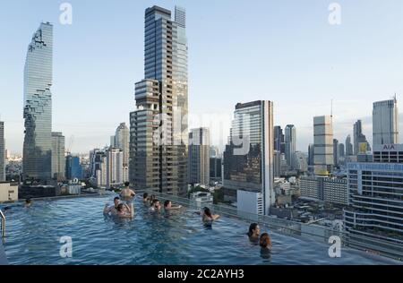 Les jeunes profitent du coucher de soleil sur les gratte-ciels de la ville, depuis une piscine à débordement sur le toit, à Bangkok. Banque D'Images