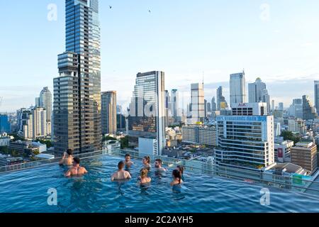 Les jeunes profitent du coucher de soleil sur les gratte-ciels de la ville, depuis une piscine à débordement sur le toit, à Bangkok. Banque D'Images