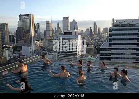 Les jeunes profitent du coucher de soleil sur les gratte-ciels de la ville, depuis une piscine à débordement sur le toit, à Bangkok. Banque D'Images