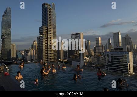 Les jeunes profitent du coucher de soleil sur les gratte-ciels de la ville, depuis une piscine à débordement sur le toit, à Bangkok. Banque D'Images