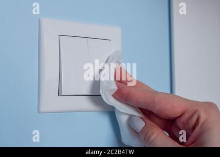 Femme mains nettoyant interrupteur lumière blanche sur mur bleu avec un désinfectant antiseptique humide. Désinfection, protection, prévention, travaux ménagers, COVID 19 Banque D'Images