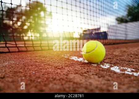 Vue rapprochée de balle de tennis près du filet, sur rouge artificiel de tennis. Banque D'Images