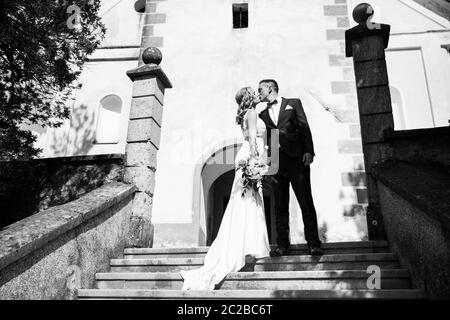 Le Baiser. Mariée et le marié embrasse tendrement sur un escalier en face d'une petite église locale. Couple de mariage élégant. Photo en noir et blanc. Banque D'Images