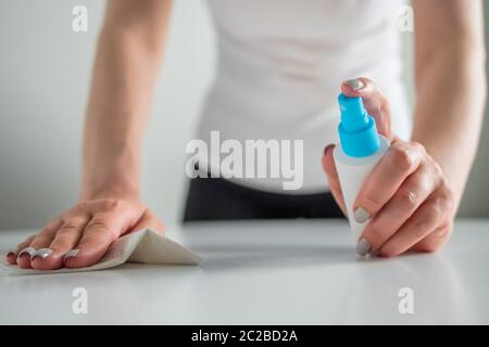 Femme mains pulvérisation antiseptique, nettoyage table blanche avec désinfectant humide lingette - gros plan. Désinfection, protection, prévention, travaux ménagers Banque D'Images