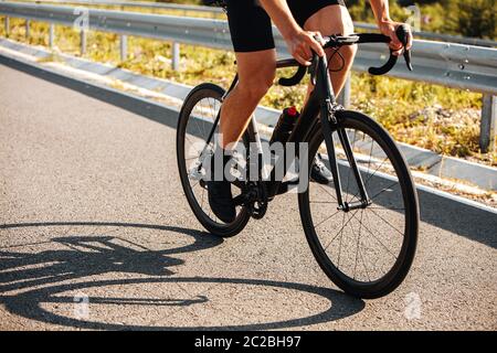 Gros plan des jambes des cyclistes dans des vêtements de sport et des baskets qui font activement du vélo professionnel sur route pavée. Homme mature qui apprécie le passe-temps en plein air. Banque D'Images