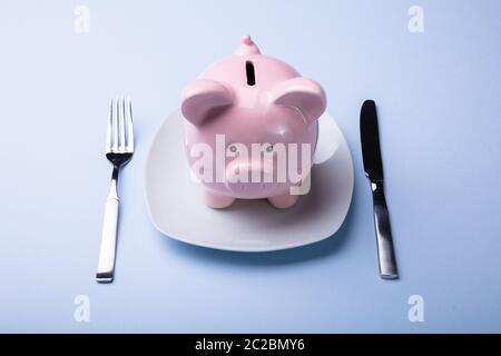 Portrait de Pink Piggy Bank sur la plaque blanche avec fourchette et couteau Banque D'Images