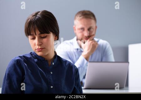 Angry Businesswoman Sitting in front of Stressed Businessman à contre fond gris Banque D'Images
