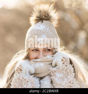 Portrait d'une jolie jeune femme à cheveux longs chapeau beige avec pompon en fourrure, foulard chaud, manteau, gants blancs couverts de neige par temps ensoleillé. FEMA Banque D'Images