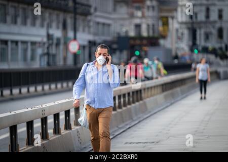 LONDRES, ANGLETERRE - 27 MAI 2020 : homme moyen-oriental d'âge moyen marchant le long du pont de Waterloo à Londres, Angleterre, portant un masque facial et parlant sur lui Banque D'Images