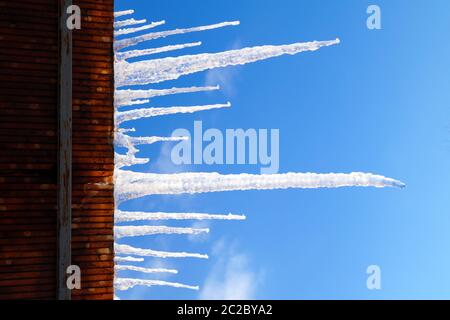 De nombreuses glaces, grandes et pointues, pendent sur le toit de la maison. Banque D'Images