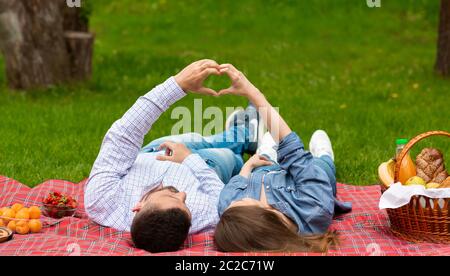 Jeune couple aimant faisant des coeurs avec leurs mains tout en étant allongé sur une couverture de pique-nique à l'extérieur Banque D'Images