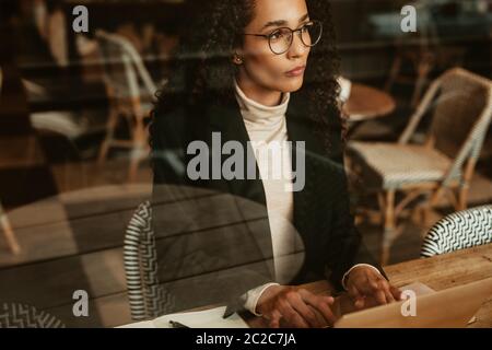 Femme d'affaires au café travaillant sur un ordinateur portable et regardant loin de penser. Femme professionnelle travaillant dans un café. Banque D'Images