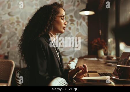 Femme d'affaires ayant une vidéoconférence sur son ordinateur portable. Vue latérale d'une femme assise au café ayant une conversation vidéo sur son ordinateur portable. Banque D'Images
