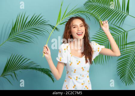 Portrait de beauté d'une femme souriante posant avec des feuilles vertes sur fond bleu Banque D'Images