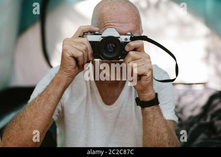 Gros plan d'un homme senior assis à l'extérieur de sa tente de camping et photographiant avec un appareil photo numérique. Homme à la retraite prenant quelques instantanés pendant le camping à natur Banque D'Images