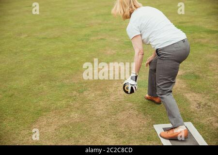 Une vue arrière vue d'un senior woman holding a boules lyonnaises, prêt à prendre sa balle dans un jeu de bowling sur gazon. Banque D'Images