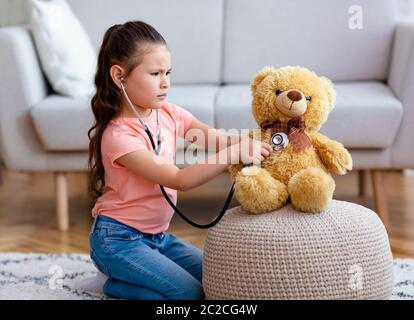 Asian Girl jouant Docteur traitant Teddy Bear Toy à la maison Banque D'Images