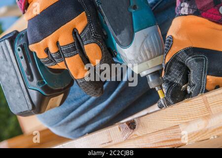 Petit jardin en bois avec perceuse visseuse sans fil dans une main. Hommes fixant des poutres en bois les uns aux autres. Thème de la maison et du jardin. Banque D'Images