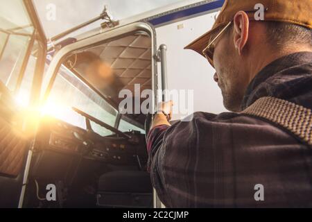 Chauffeur de camion caucasien professionnel dans ses années 40 entrer dans sa cabine de camion. Thème transport lourd. CDL Drive. Banque D'Images