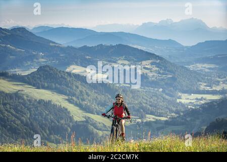 Jolie femme âgée à cheval sur son vélo électrique de montagne sur les montagnes au-dessus d'Oberstaufen, Allgau Alpes, Bavière Allemagne Banque D'Images