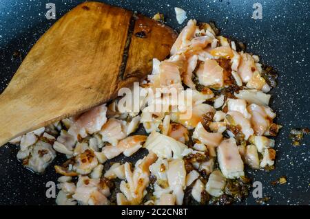 Cuisson des oignons rouges émincés et du saumon fumé à l'huile d'olive sur une poêle en gros plan. Banque D'Images