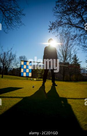 Golfeur sur le vert de mise et tenant le drapeau de golf avec la lumière du soleil. Banque D'Images