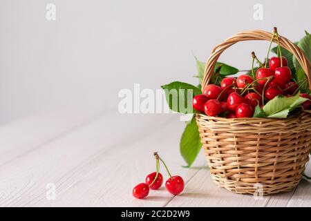 Cerises mûres juteuses dans un panier en osier sur fond de bois blanc Banque D'Images
