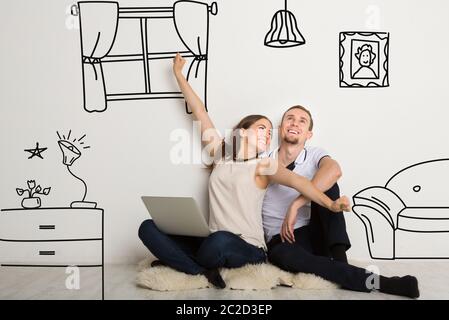 Bonne fille avec petit ami imaginer leur nouvel intérieur de maison, collage avec des dessins de meubles de Doodle sur le mur blanc Banque D'Images