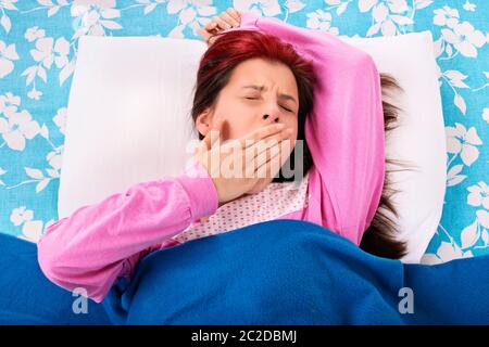 Belle jeune fille couchée sur un coussin sous une couverture de bâiller, isolé sur un fond blanc. Banque D'Images