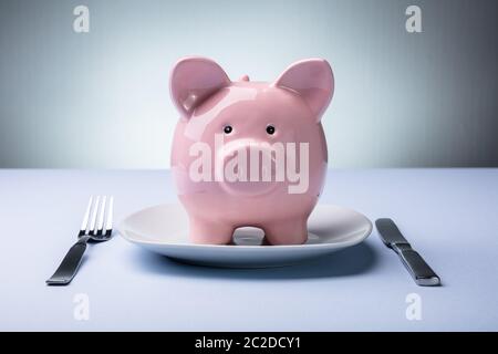 Portrait de Pink Piggy Bank sur la plaque blanche avec fourchette et couteau Banque D'Images