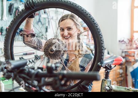 Très heureux mécanicien vélo femme regardant à travers la roue de bicyclette Banque D'Images