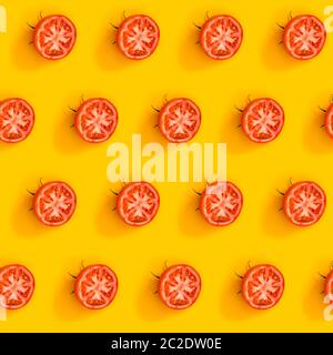 Motif diagonal de tomates mûres juteuses coupées en deux sur fond jaune vif. Flat lay minimaliste et créatif. Vitamines vegan concept de régime sain. Banque D'Images