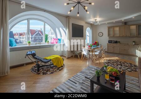 Intérieur moderne du salon dans un studio de luxe. Fenêtre semi-cercle. Chaise longue. Ensemble cuisine. Définir la table. Banque D'Images