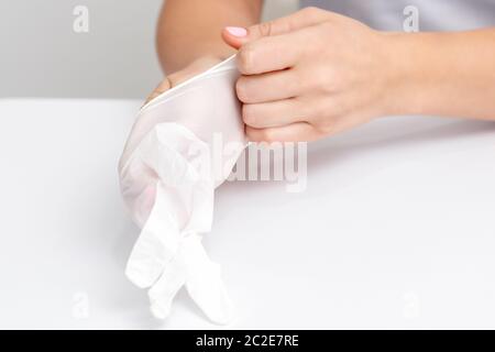 Les mains des femmes mettent les gants en caoutchouc blanc dans un salon de manucure. Banque D'Images