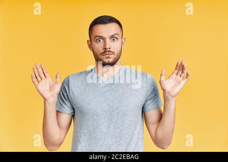 Un jeune homme choqué avec des bras vers le haut, regardant stupéfait dans l'appareil photo sur fond jaune Banque D'Images