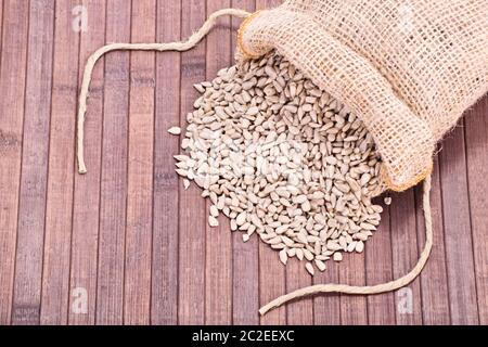 Gros plan de graines de tournesol en sac de jute renversé sur un fond de bois. Banque D'Images