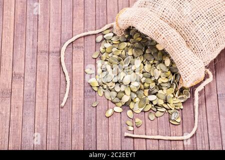 Rapprochée sur les graines de citrouille déversés par un sac de toile, sur un fond de bois. Banque D'Images